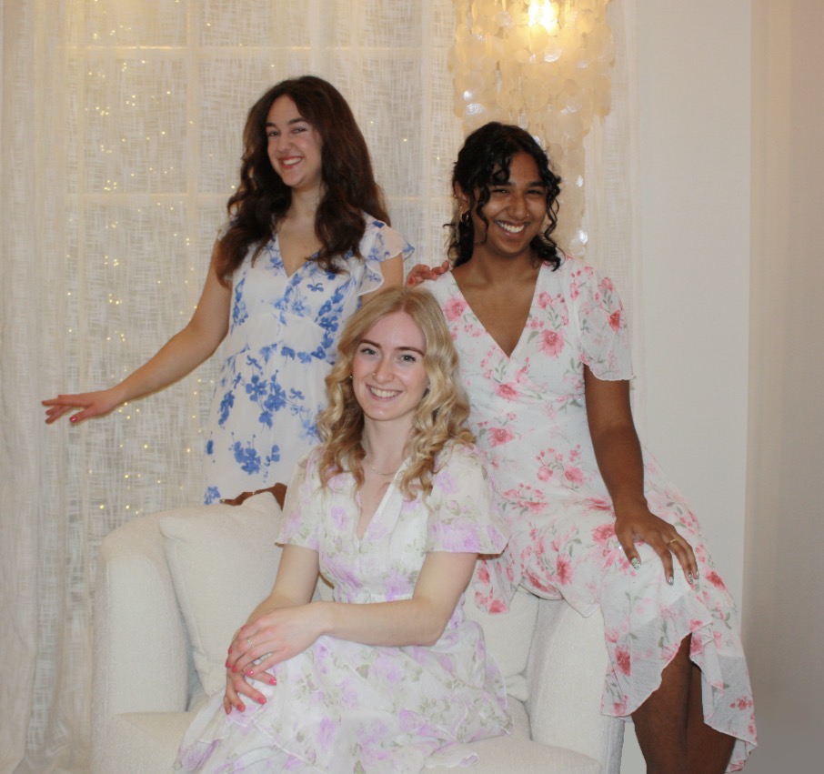 members of the petit-tones vocal trio Paulina Salisbury, Emma Gillingham and Sanjana Brijlall in floral dresses with a light shining behind.