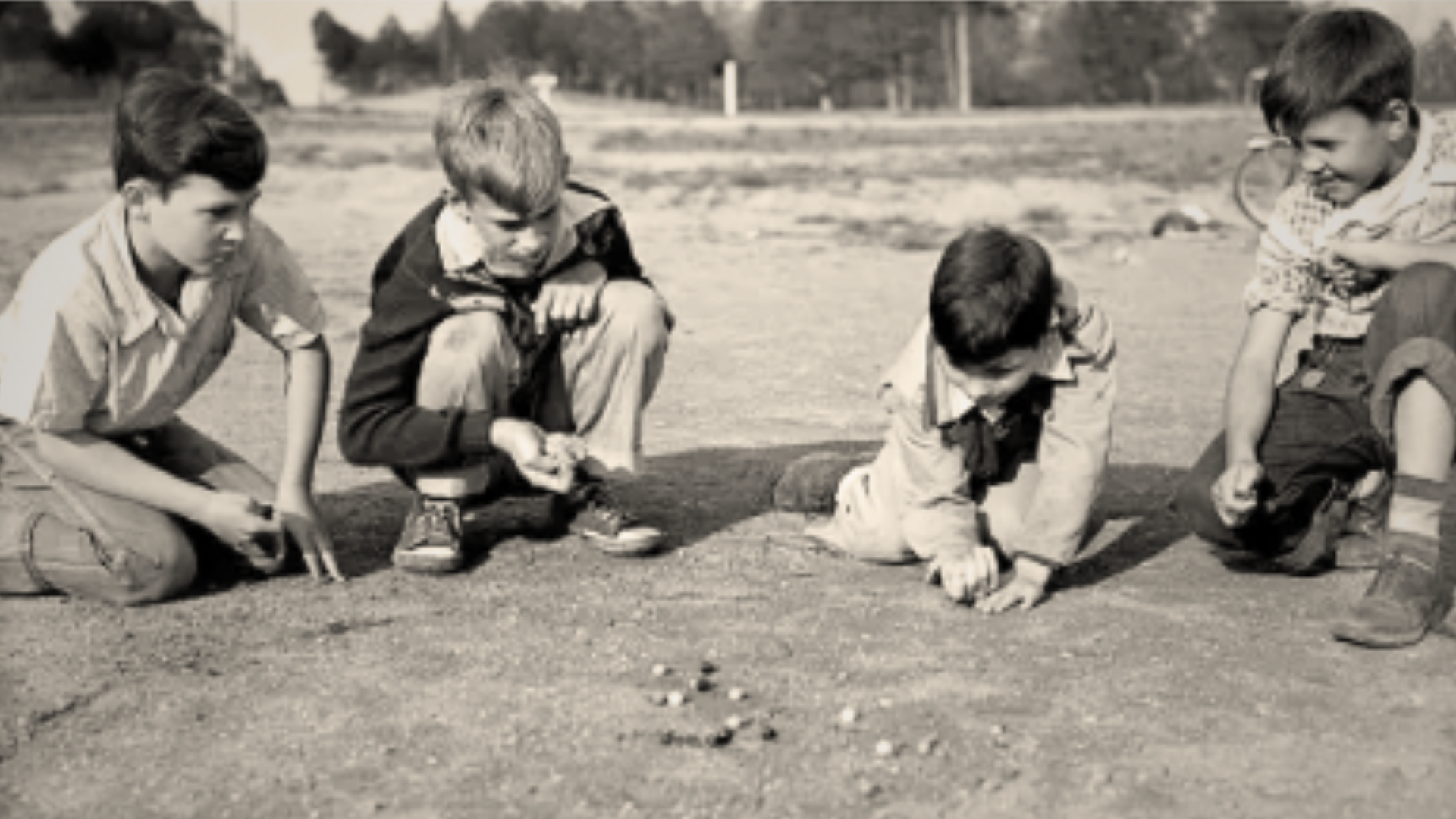 four boys playing jacks outside 