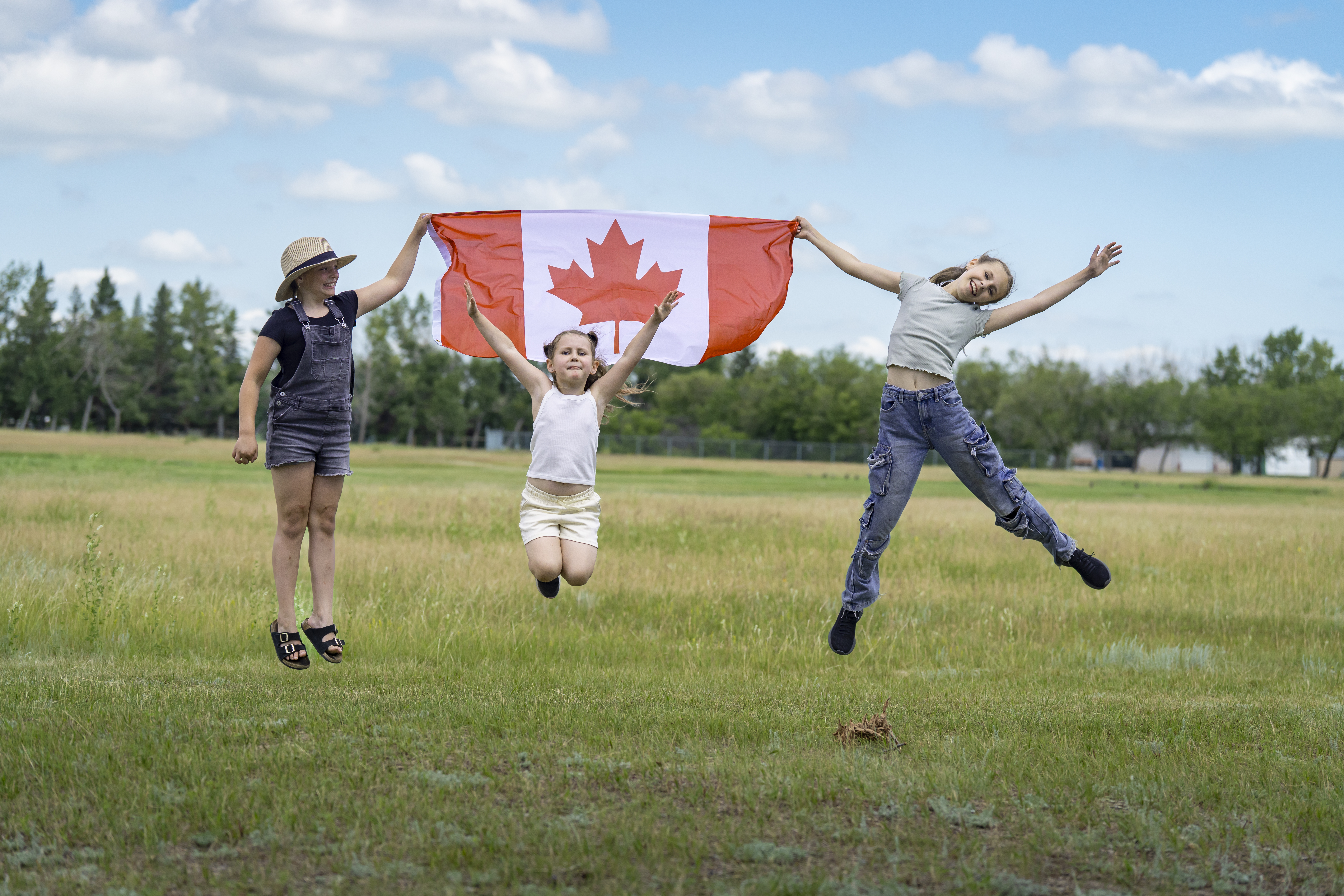 Three youth jump holding a Canada flag.