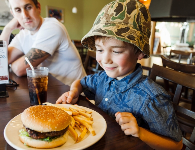 A young boy looking and smiling at a hambuger 