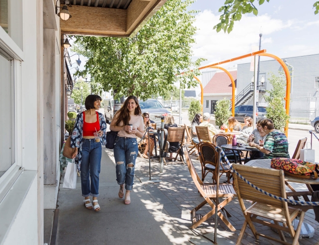 Two women walking along a busy street with patio tables lining the sidewalk