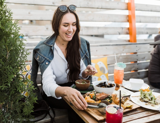 a woman sitting outdoors on a patio at a table set with dinner and cocktails