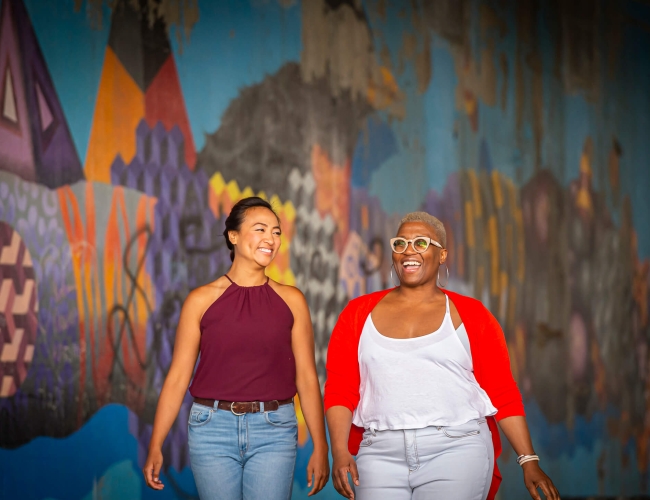 two women walking downtown in front of an art wall