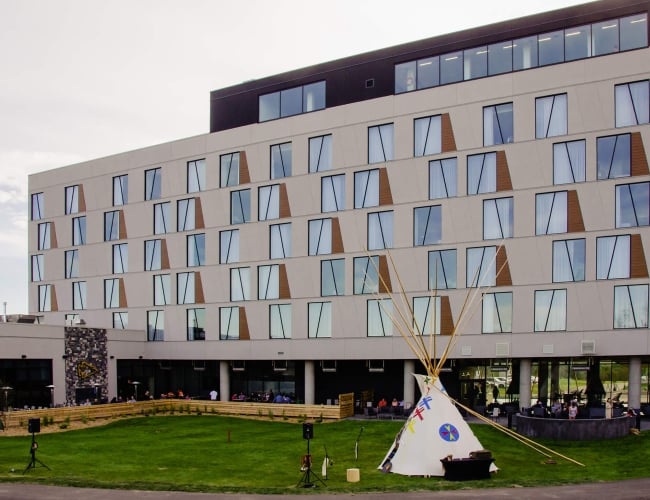External of a brick building with a green lawn and a teepee on the lawn