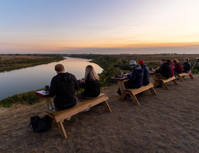 couples sitting outdoors at multiple tables overlooking a river at sunset