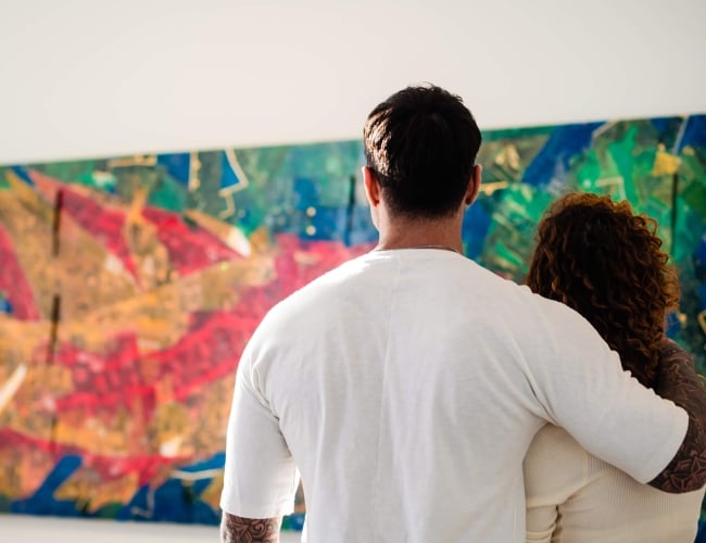 man with his arm around a woman looking at a large piece of artwork