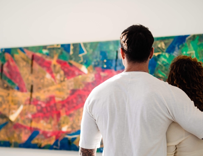 man with his arm around a woman looking at a large piece of artwork