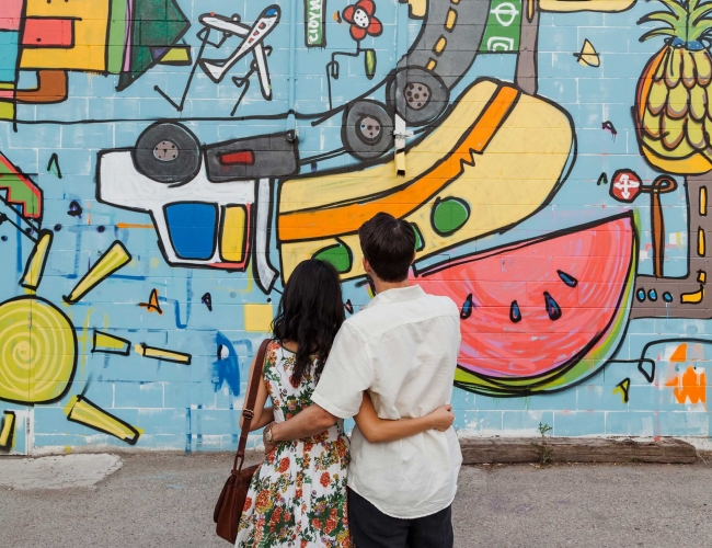 A couple hugging while looking at a painted mural wall