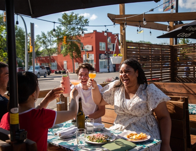 four individuals sitting at an outdoor table on a restaurant table "cheersing" drinks