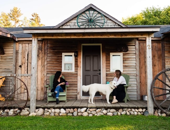 Two women sitting on the porch of a log cabin with a dog