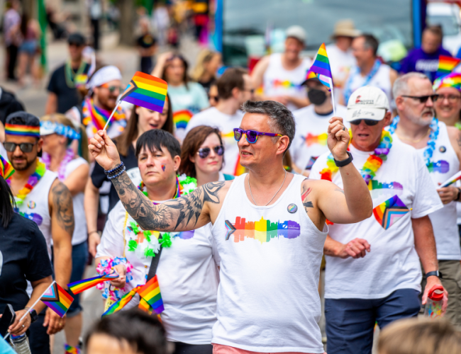 Person walking in a pride parade waving two progressive pride flags