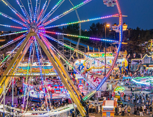 Fair ground at night with a big Ferris wheel in the middle.