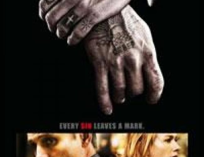 Image from the movie eastern Promises with a man holding his wrist, wearing  a black suit and an expensive watch. His hands are covered in tattoos. 