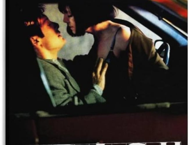 Image from the movie; Crash. Shows a woman on top of a man in a car with implication that they are about to kiss.