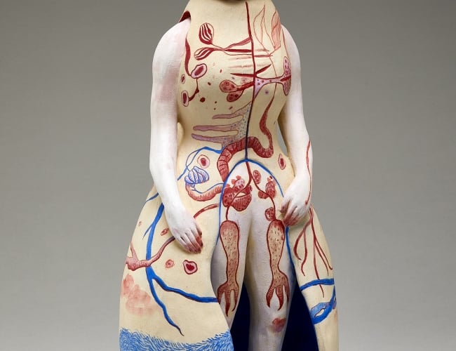 "Anasyrma" by Maia Stark, a clay sculpture of a human figure, wearing a long cream dress with red and blue details.