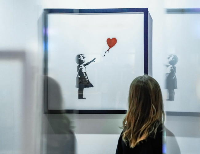 Person looking at a Banksy painting of a girl with a balloon.