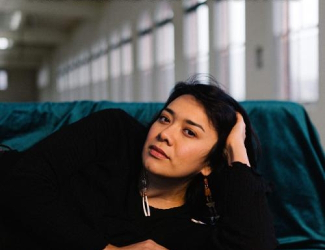 Image of Black Belt Eagle Scout Kathrine Paul Laying on her side on a couch in a long hallway. Text is written: Black Belt Eagle Scout September 30 The Broadway Theatre Tickets at broadwaytheatre.ca