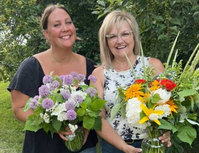 Two women stand outside at Black Fox Farm and Distillery holding flower arrangements after attending a flower class.