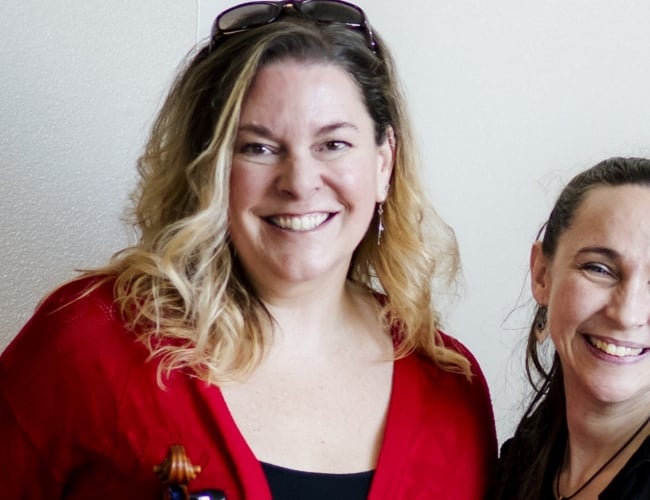 Kim de Laforest in Red holding a violin, with Anna Marie Bekolay both smiling