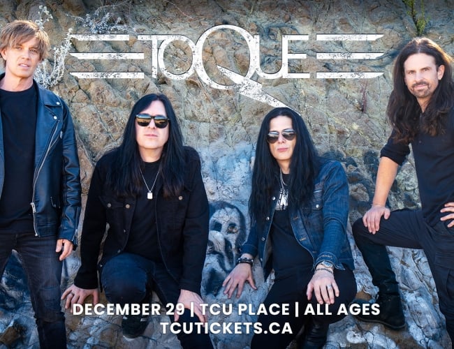 An image of four men, TOQUE, posing in front of a rock. 