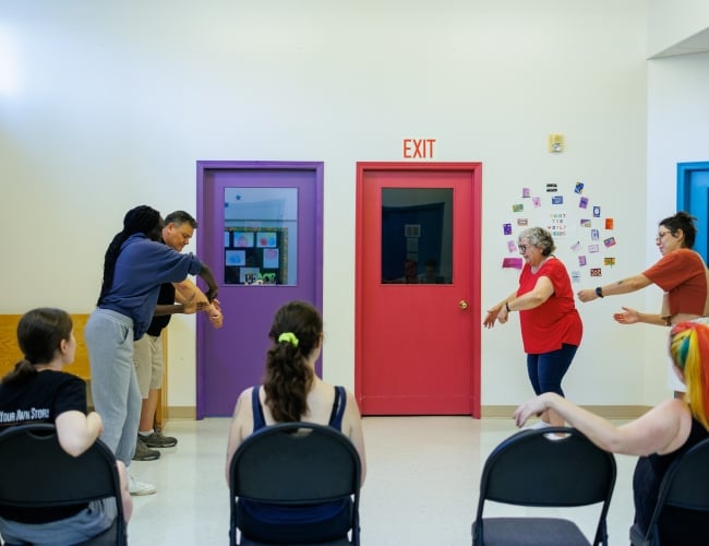A group of people in a classroom playing improv games in front of other students in the class.