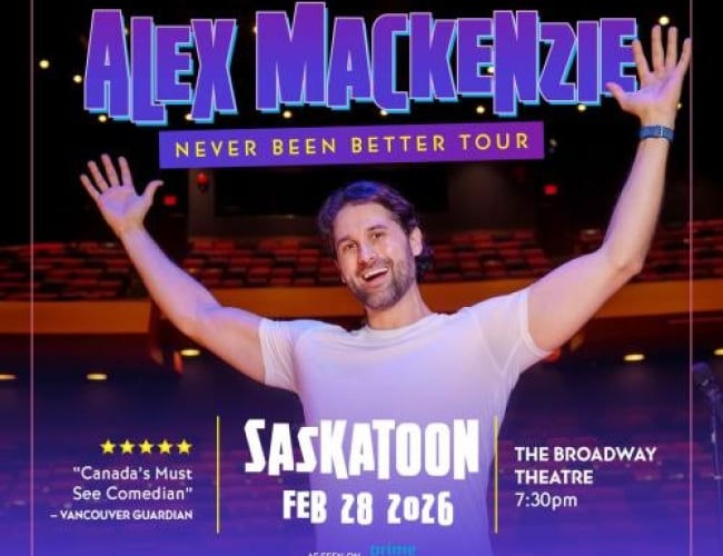 Image of Comedian Alex MacKenzie with his arms up and smiling. Behind him is a large theatre with red seats. 