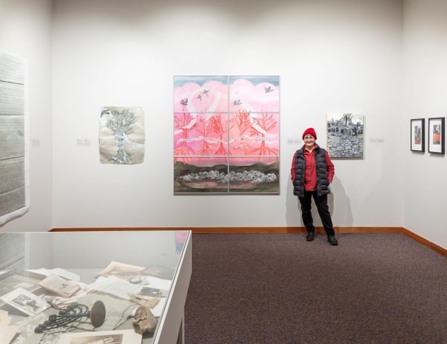 Image of the artist Betsy Rosenwald standing next to one of her paintings titled Homage in the museum's gallery.