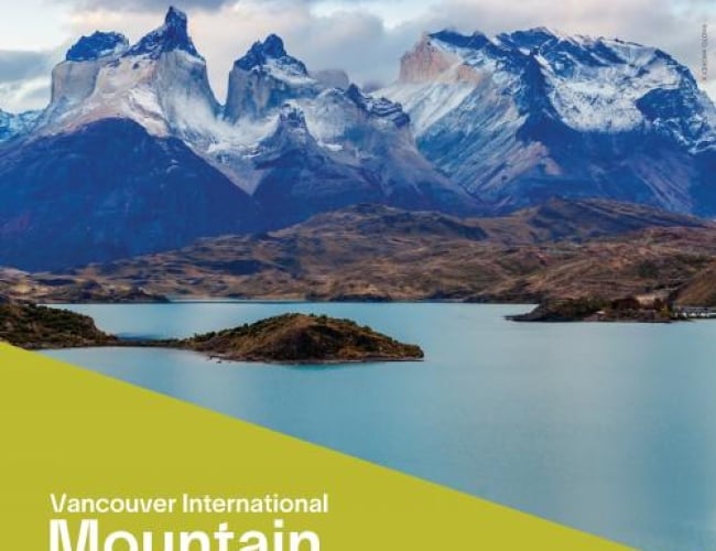 Image of snowy mountains with clear blue lake and dark clouds overhead.