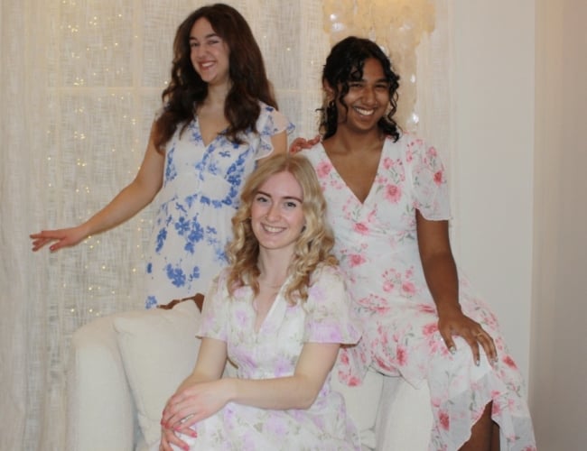 members of the petit-tones vocal trio Paulina Salisbury, Emma Gillingham and Sanjana Brijlall in floral dresses with a light shining behind.