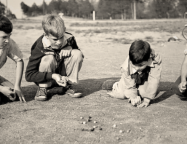 four boys playing jacks outside 
