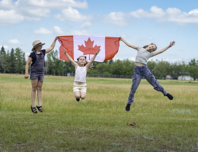 Three youth jump holding a Canada flag.