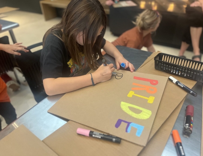 Youth participating in making pride signs using colourful markers on cardboard.