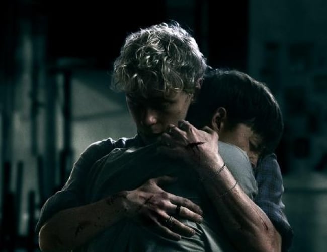 Image of two boys hugging eachother with cuts all over their arms, standing in the dark.