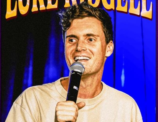 Image of comedian Luke Kidgell holding a mic and looking off into the audience. 