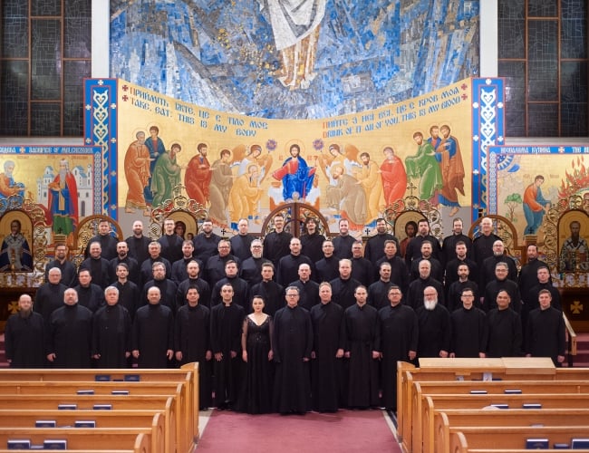 The Axios Men's Ensemble of over 50 performers in church, arranged in front of a Christian mural.
