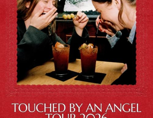 Image of two women laughing at a table over caesar drinks with olives. 