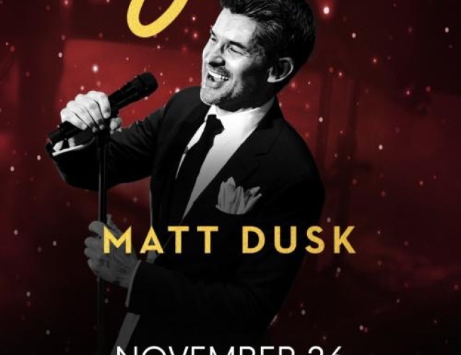 Image of Matt Dusk in a black and white photo, smiling in front of a mic.