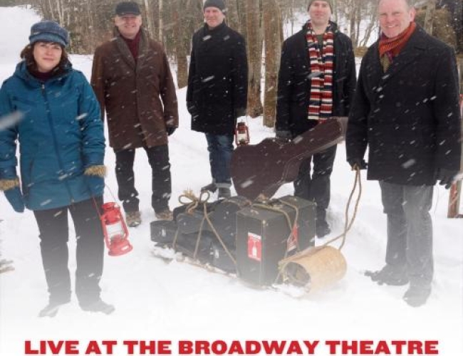 Image of the band the Barra MacNeils standing in snow and wearing winter clothes, with instruments on a sled.