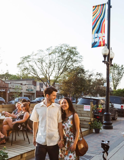 couple walking down the street holding hands but patio tables set out on the street