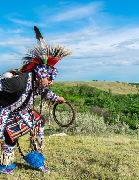 An Indigenous man dancing outside dressed in traditional beaded clothing