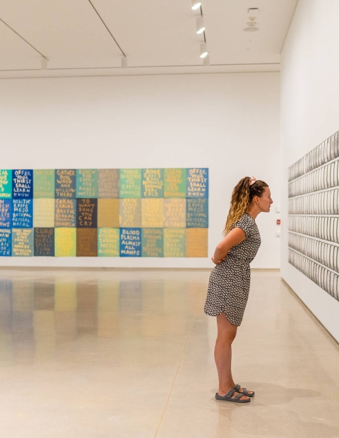 Woman with her arms behind her back, looking at art on a wall in a gallery