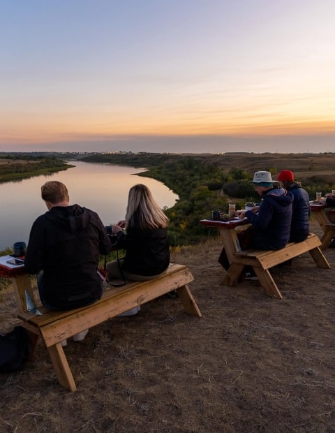 couples sitting outdoors at multiple tables overlooking a river at sunset
