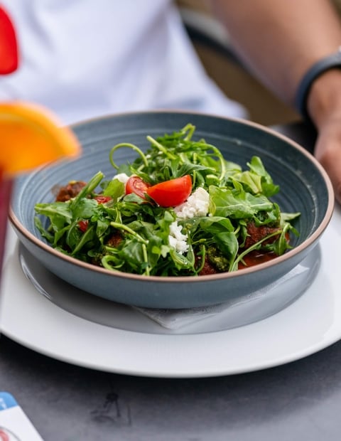 an individual sitting at an outdoor table eating a salad and drinking a cocktail