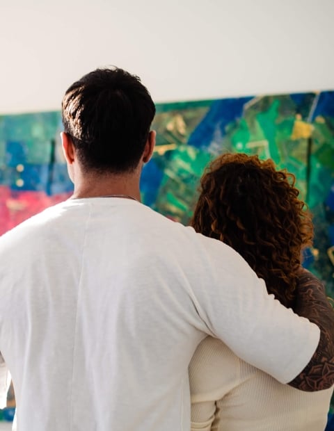 man with his arm around a woman looking at a large piece of artwork
