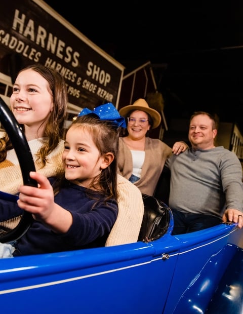 a family pretending to drive a model car in a historic museum