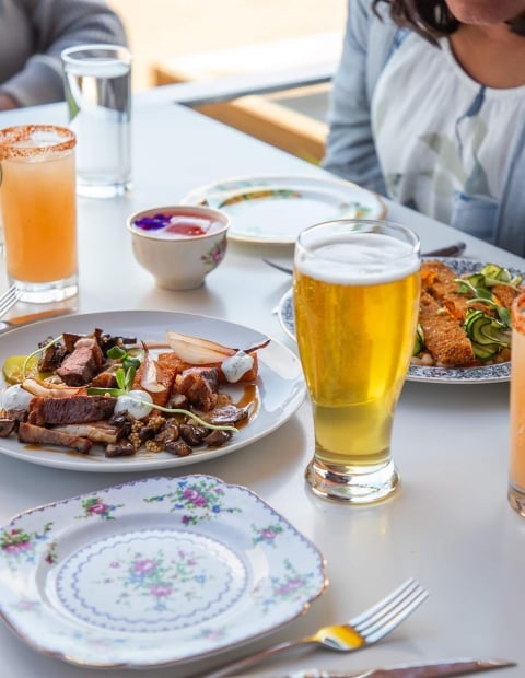 An outdoor restaurant table set with appetizers and cocktail/beer drinks