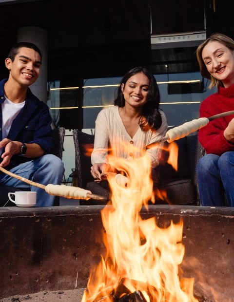 Three individuals sitting around a bonfire roasting marshmallows 