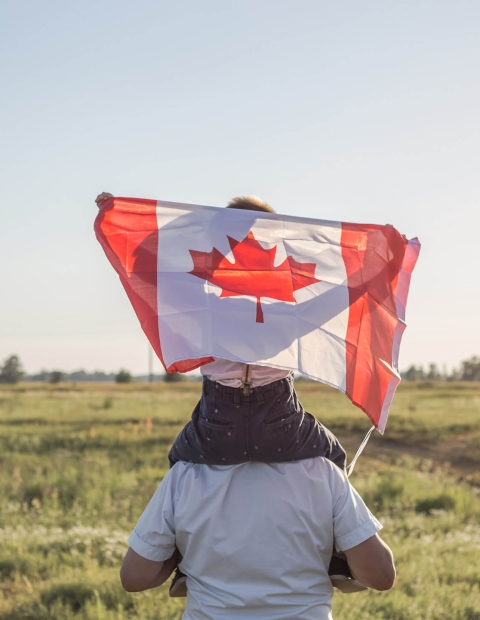 Child holding Canadian flag sitting on someones shoulders