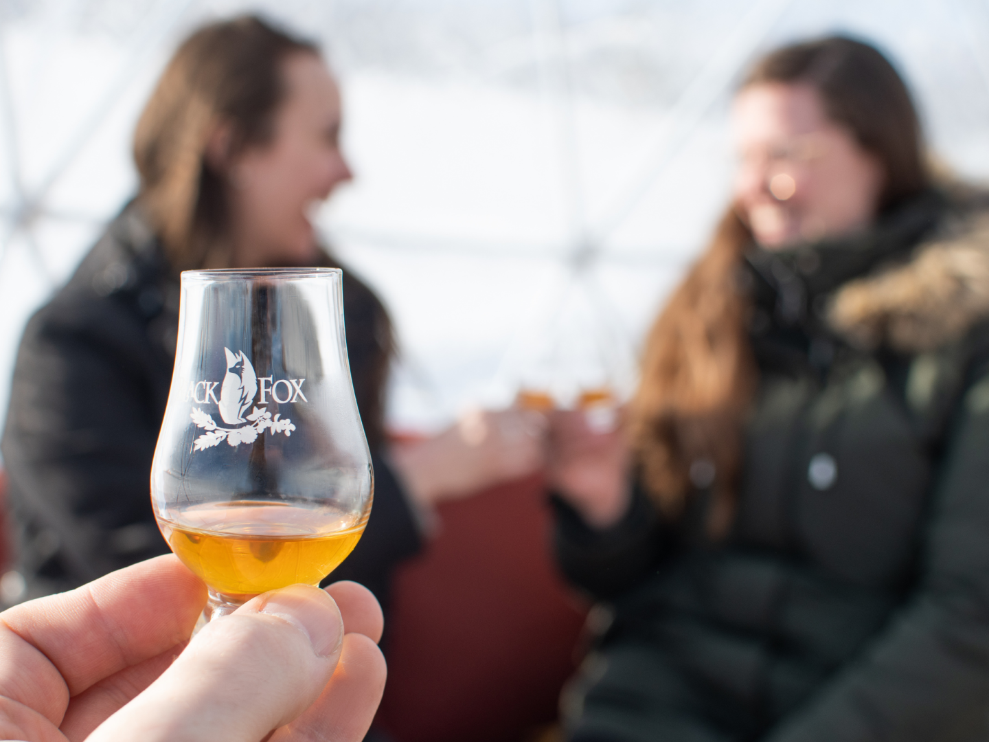 Whisky Glencairn glass filled with whisky with two smiling females celebrating event.