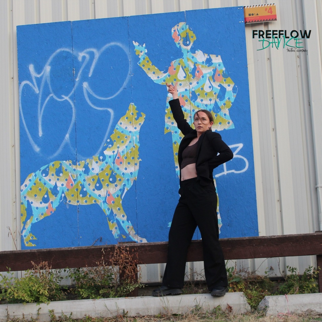 Dancer in black in front of a colourful mural of a man and dog